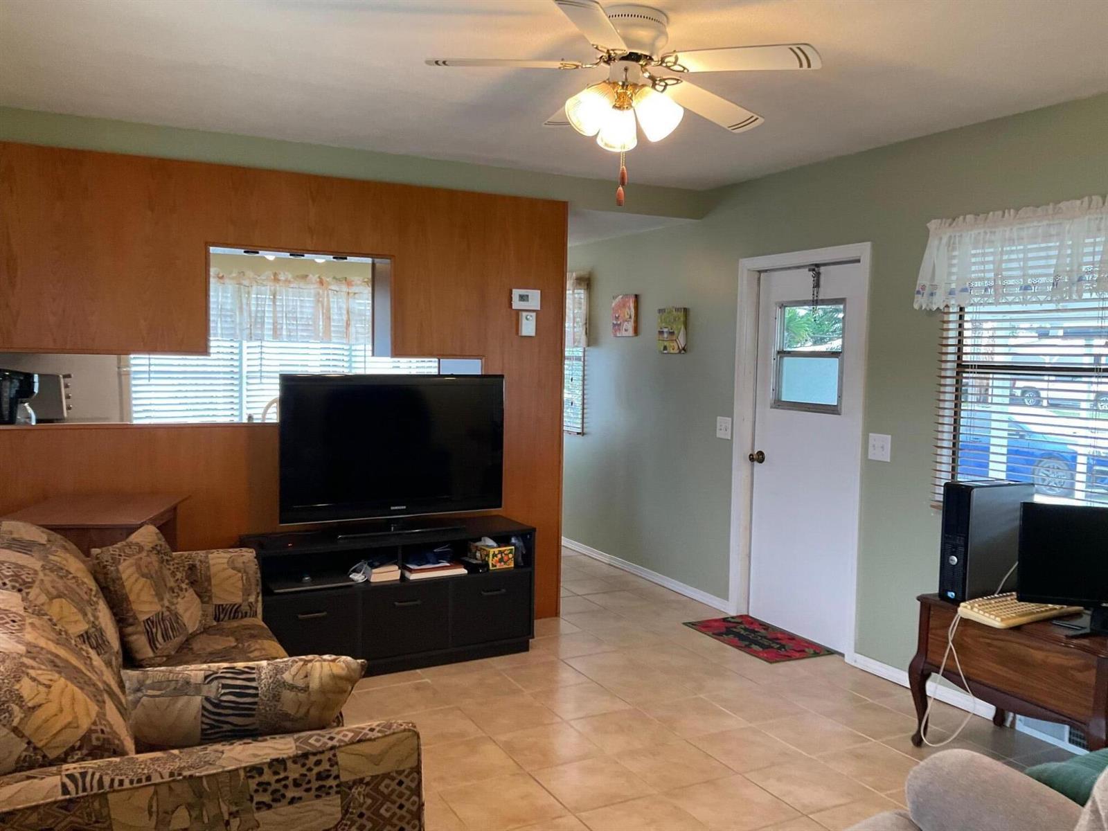 A living room features tile flooring, a ceiling fan, a wood-paneled wall, and an exterior door — 1601 Us, Okeechobee FL 34974, OKEECHOBEE, FL