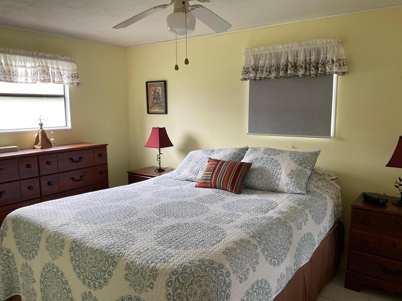 A bedroom features light yellow walls, a queen bed with patterned bedding, and wooden furniture — 1601 Us, Okeechobee FL 34974, OKEECHOBEE, FL