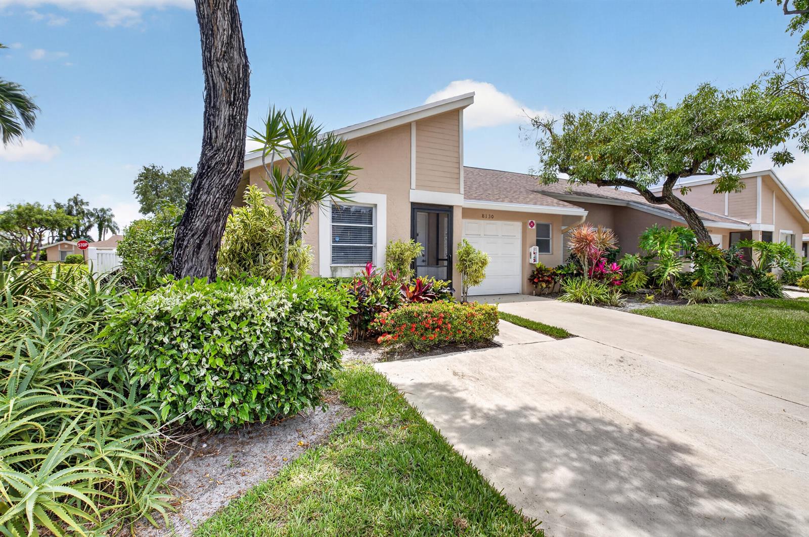 A tan single-story house with a white garage door and lush landscaping under a blue sky — 8130 Springtree Road # A, Boca Raton FL 33496, BOCA RATON, FL