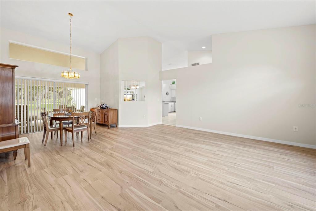A spacious dining and living area features light wood flooring, vaulted ceilings, and sliding doors — 432 MISTWOOD COURT, SPRING HILL, FL