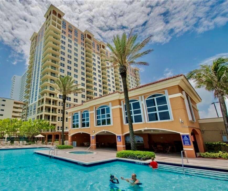 A swimming pool with people in the water sits before a tall residential building — 2080 S Ocean Drive, Hallandale Beach FL 33009, HALLANDALE BEACH, FL