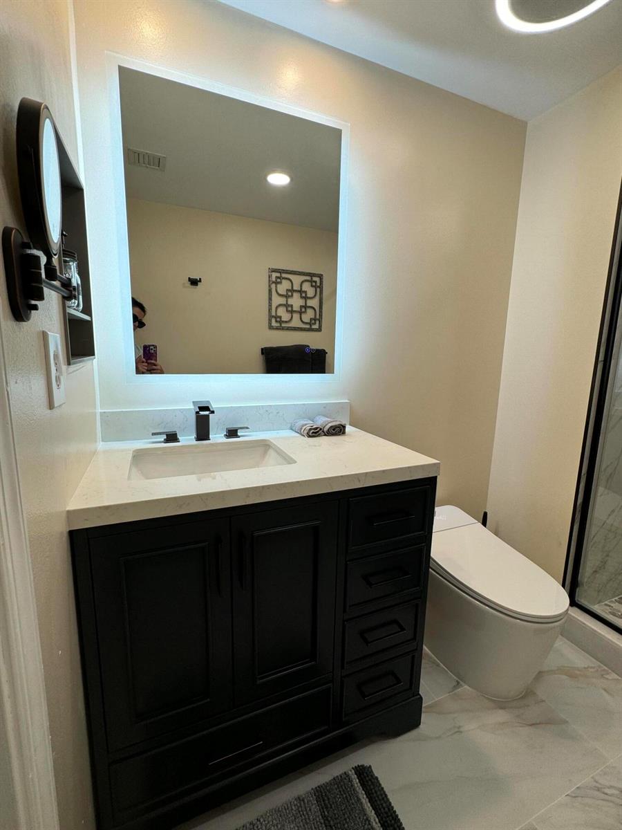 A bathroom features a dark vanity with a white countertop, a backlit mirror, and toilet — 2080 S Ocean Drive, Hallandale Beach FL 33009, HALLANDALE BEACH, FL