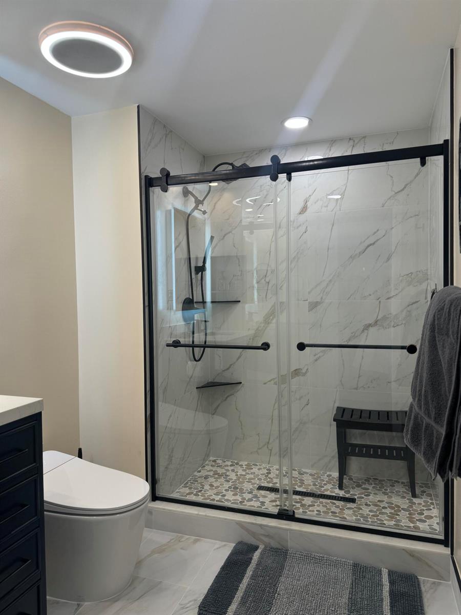 A bathroom features a walk-in shower with marble-look tile, pebble flooring, and black hardware — 2080 S Ocean Drive, Hallandale Beach FL 33009, HALLANDALE BEACH, FL