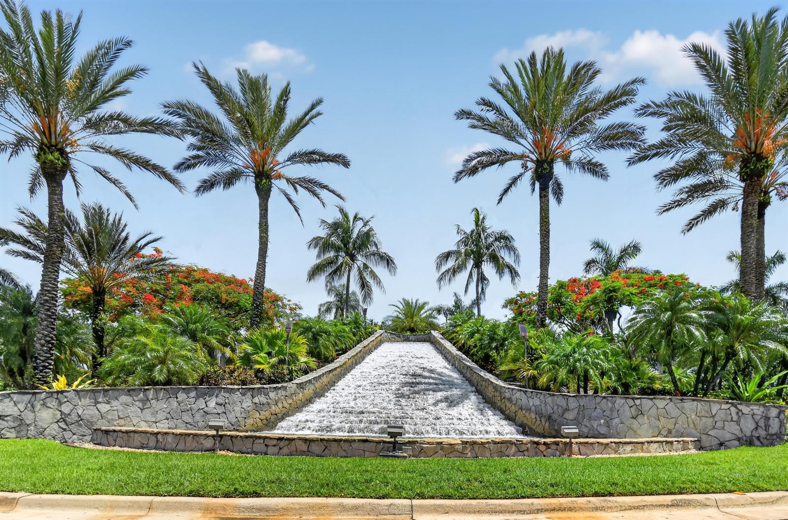 A stone-walled water feature cascades down a landscaped hill surrounded by tall palm trees — 9442 Bridgeport Drive, West Palm Beach FL 33411, WEST PALM BEACH, FL