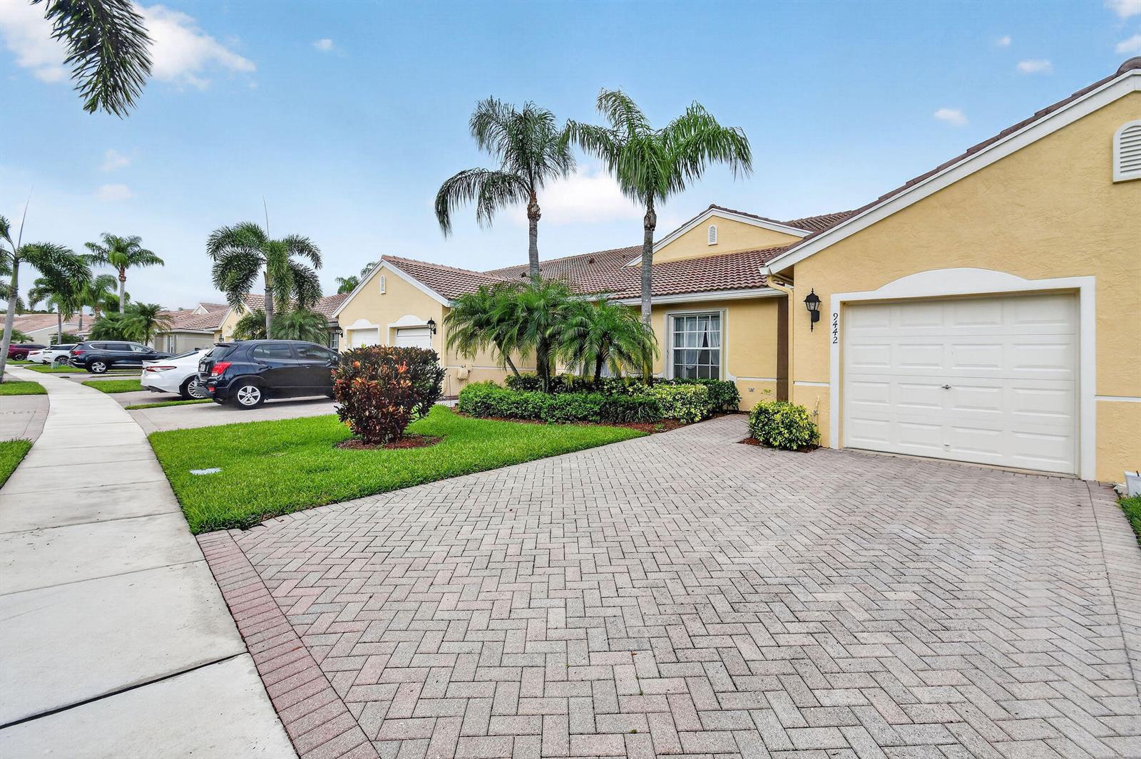 A yellow single-story house with a paved driveway, a garage, and palm trees — 9442 Bridgeport Drive, West Palm Beach FL 33411, WEST PALM BEACH, FL