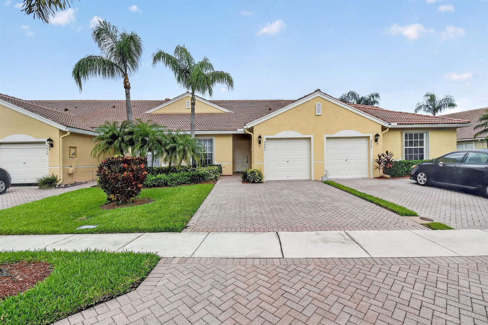 A yellow single-story house with a tiled roof, two garage doors, and a paved driveway — 9442 Bridgeport Drive, West Palm Beach FL 33411, WEST PALM BEACH, FL