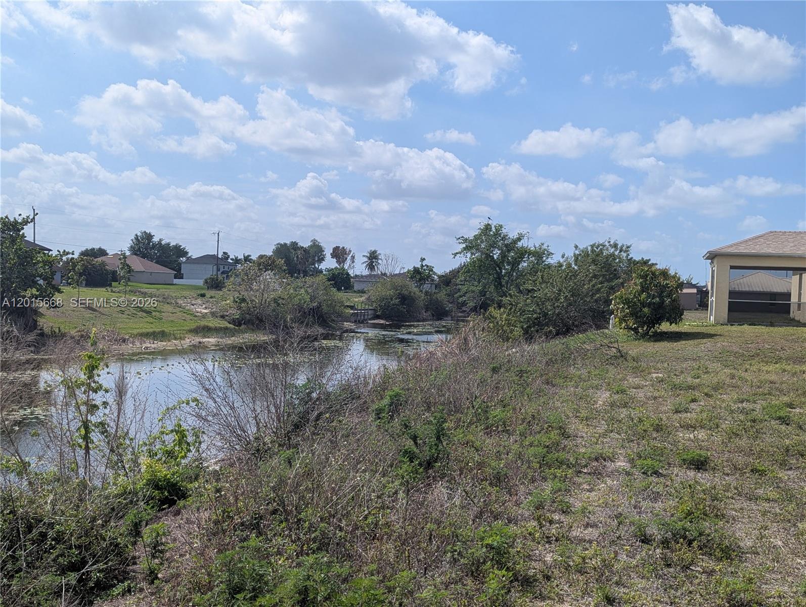 A view of a grassy lot bordering a small canal with trees and houses nearby — 1402 NE 14 ave, Cape Coral FL 33909, CAPE CORAL, FL
