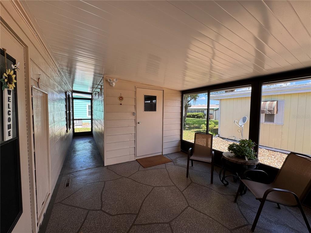 A covered porch features a textured concrete floor, screen walls, and a light-colored door — 6733 KENSINGTON DRIVE NE, WINTER HAVEN, FL