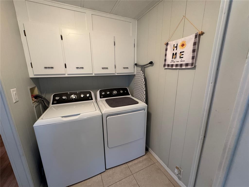 A laundry room features white cabinets, a washer, a dryer, and an ironing board — 6733 KENSINGTON DRIVE NE, WINTER HAVEN, FL