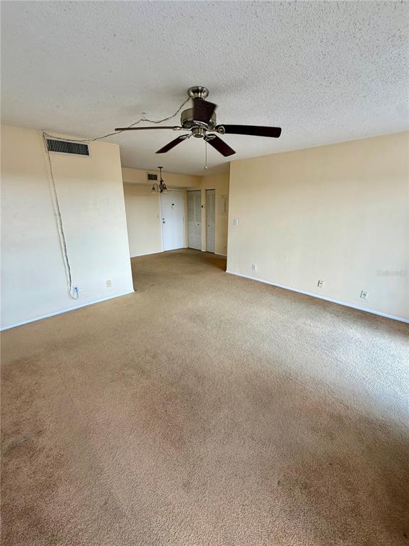 An empty living room features beige carpeting, a ceiling fan, and a white entry door — 2901 26TH STREET W UNIT 617, BRADENTON, FL