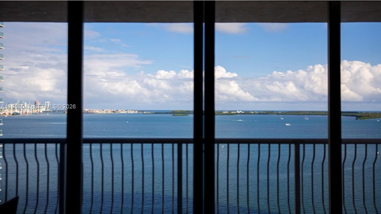 A view of a bay and distant city skyline seen through a glass balcony door — 1200 Brickell Bay Dr # 1901, Miami FL 33131, MIAMI, FL