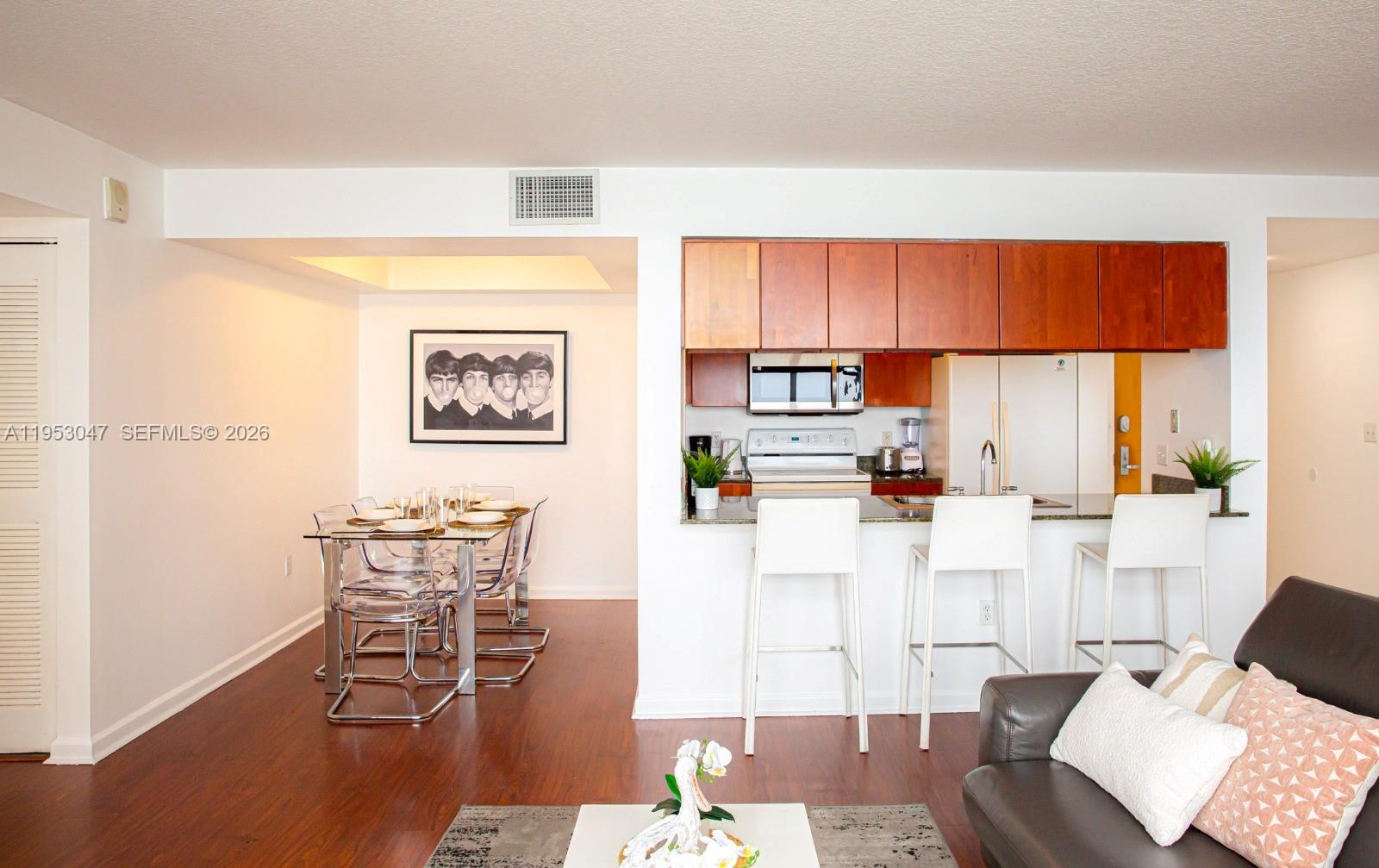 A dining area and kitchen with wood cabinets, white bar stools, and a glass table — 1200 Brickell Bay Dr # 1901, Miami FL 33131, MIAMI, FL