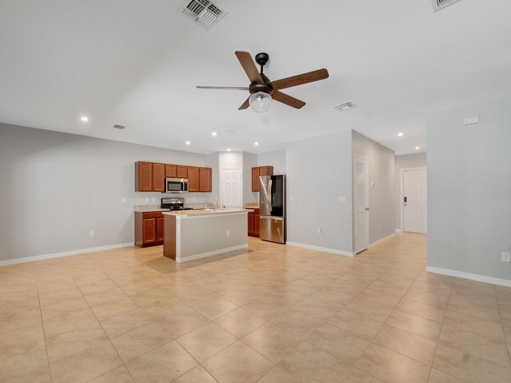 A kitchen with wood cabinets and stainless steel appliances opens to a large tiled room — FORT PIERCE, FL