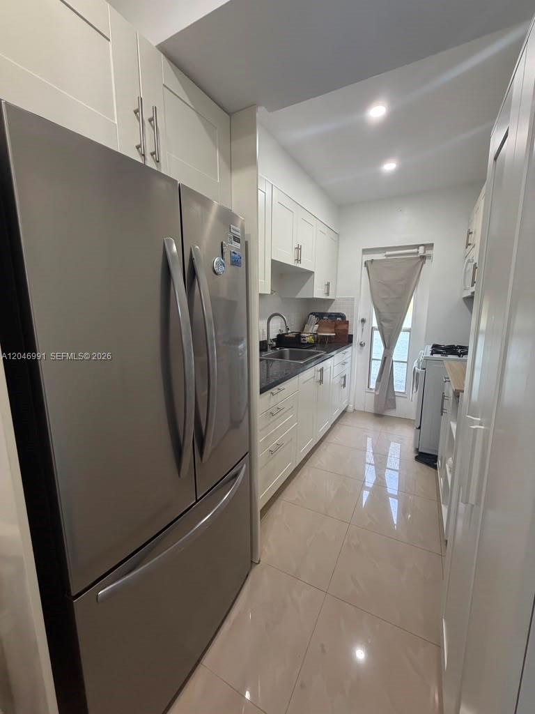 A narrow galley kitchen features stainless steel appliances, white cabinetry, and light-colored tile flooring — 8550 Byron Ave # 2H, Miami Beach FL 33141, MIAMI BEACH, FL