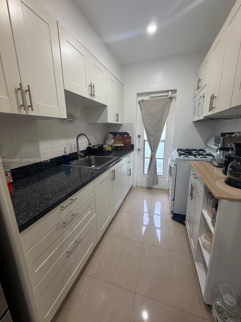 A narrow galley kitchen features white cabinets, dark granite countertops, and light tile flooring — 8550 Byron Ave # 2H, Miami Beach FL 33141, MIAMI BEACH, FL