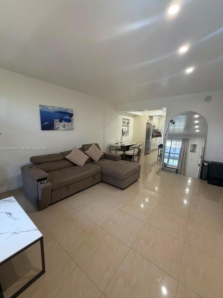A living room features a brown sectional sofa, tiled floors, and an arched floor mirror — 8550 Byron Ave # 2H, Miami Beach FL 33141, MIAMI BEACH, FL
