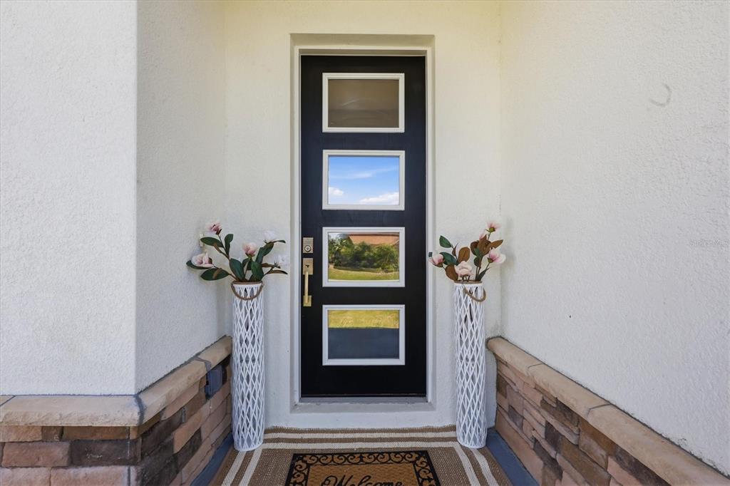 A black front door with four glass panels is flanked by two tall white vases — 12387 MINOT AVENUE, PORT CHARLOTTE, FL