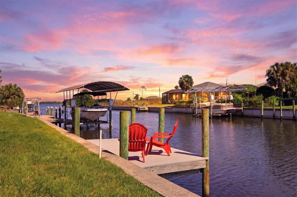A wooden dock with two red chairs sits on a canal featuring boat lifts — 12387 MINOT AVENUE, PORT CHARLOTTE, FL