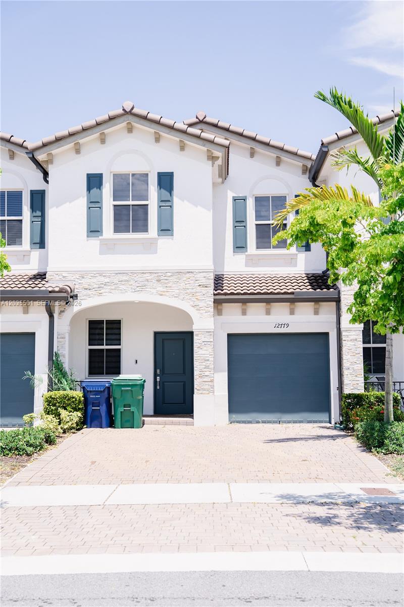 A two-story townhouse exterior features white stucco, stone accents, blue shutters, and a paved driveway — 12779 NW 24th Ave, Miami FL 33167, MIAMI, FL
