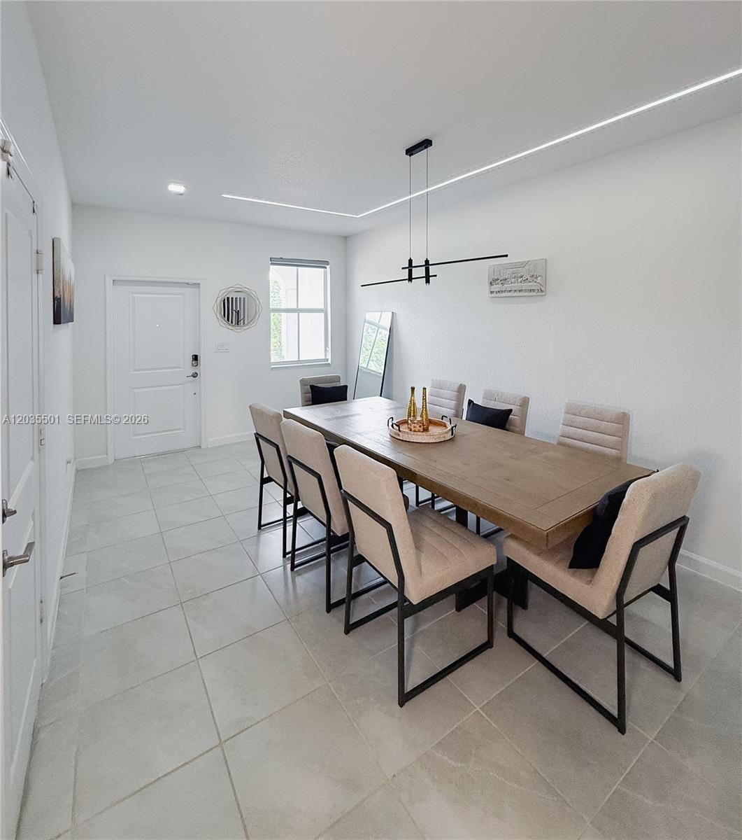 A dining room features a long wooden table, eight upholstered chairs, and modern lighting — 12779 NW 24th Ave, Miami FL 33167, MIAMI, FL