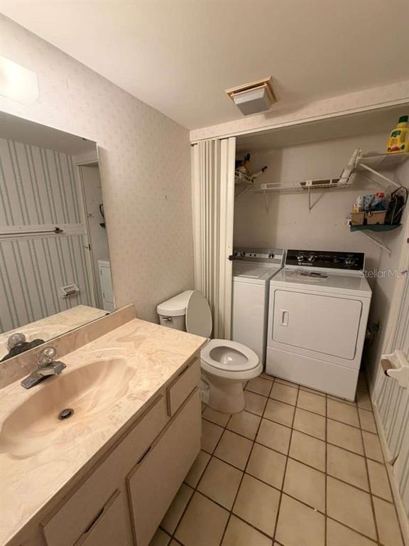 A bathroom with a vanity, toilet, and laundry appliances behind a folding door — 4150 S ATLANTIC AVENUE UNIT 126C, NEW SMYRNA BEACH, FL