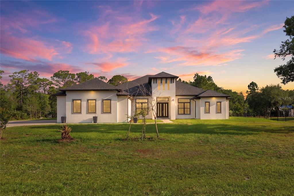 A modern single-story house with a stucco exterior and dark-framed windows sits on a lawn — 5700 BANCROFT BOULEVARD, ORLANDO, FL