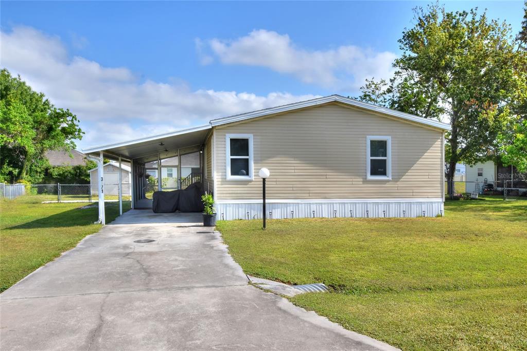 A beige mobile home with a carport and concrete driveway sits on a grassy lot — 3071 KEUKA LOOP, LAKELAND, FL