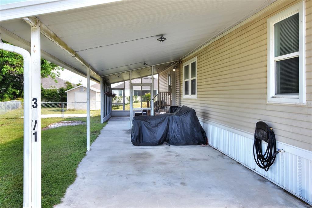 A covered concrete carport area sits beside a tan-sided home with a screened-in porch — 3071 KEUKA LOOP, LAKELAND, FL
