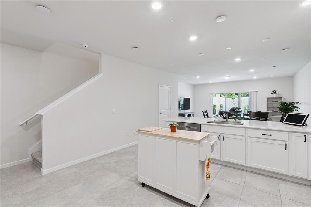 A kitchen with white cabinets, a portable island, and tile flooring opens to a living area — 1995 CANNY COVE, WINTER PARK, FL