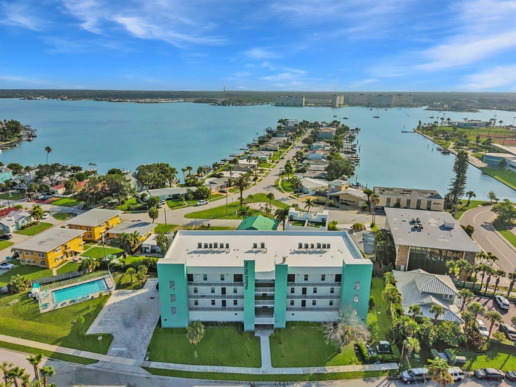 An aerial view shows a multi-story teal apartment building with a pool and waterfront homes — 15305 1ST STREET E UNIT 202, MADEIRA BEACH, FL