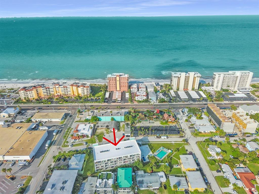 An aerial view shows a multi-story apartment building with a red arrow pointing toward it — 15305 1ST STREET E UNIT 202, MADEIRA BEACH, FL