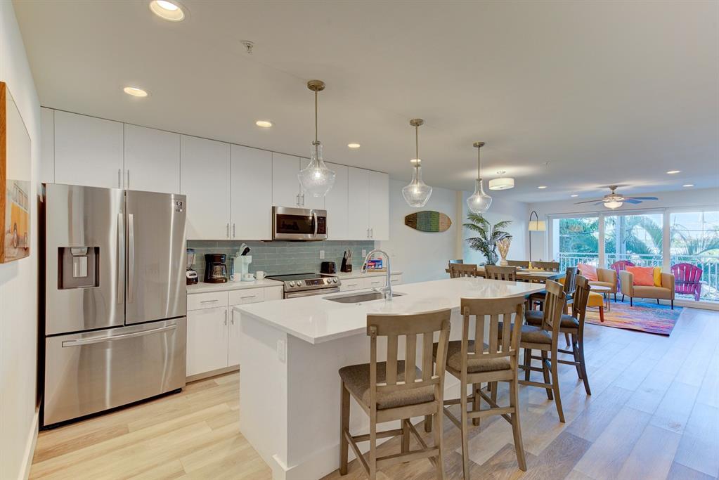 A modern kitchen with white cabinets, stainless steel appliances, and an island with bar seating — 15305 1ST STREET E UNIT 202, MADEIRA BEACH, FL