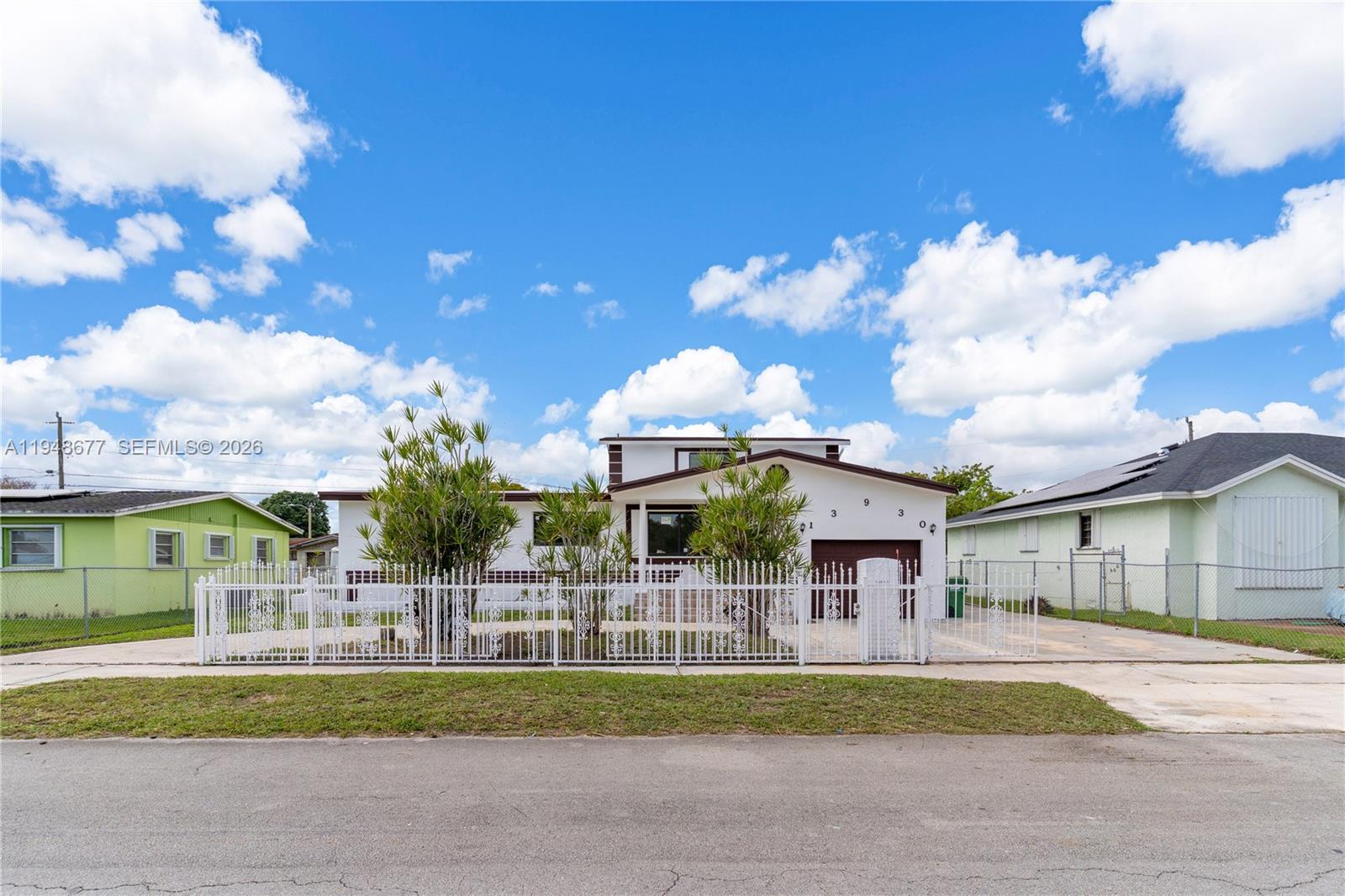 A white house with a brown garage door sits behind a white decorative metal fence — 13930 Van Buren St, Miami FL 33176, MIAMI, FL