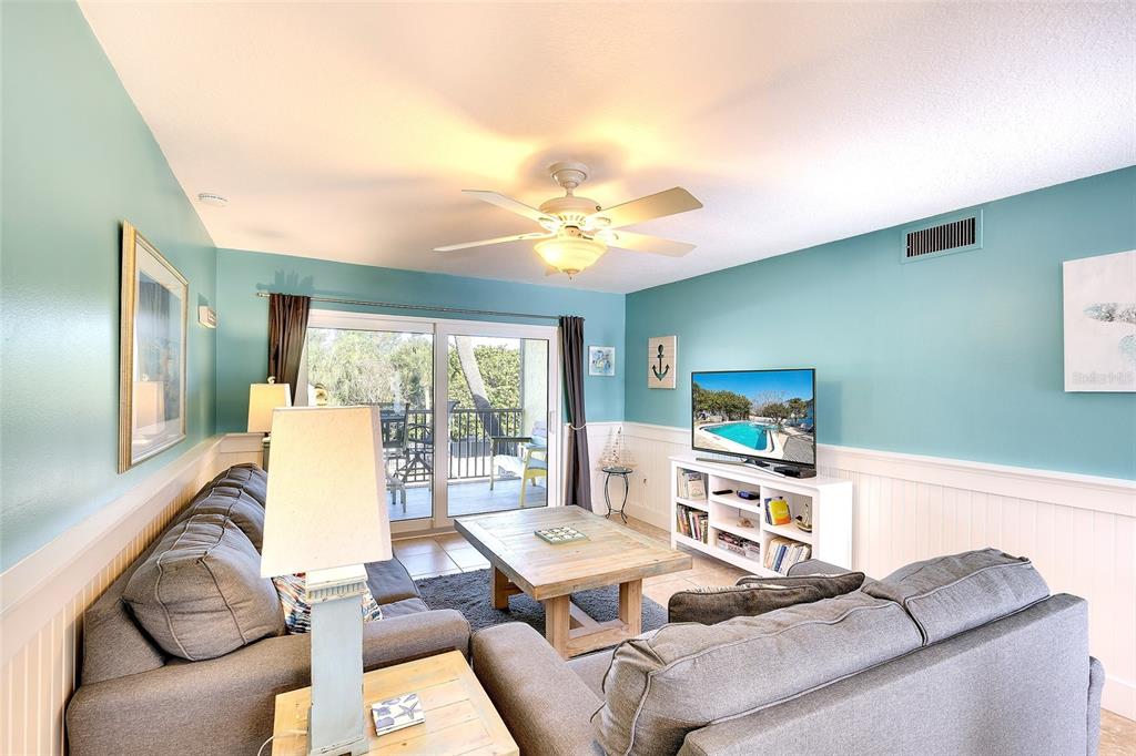 A living room features a gray sofa, a wooden coffee table, and a television stand — 4307 GULF DRIVE UNIT 207, HOLMES BEACH, FL