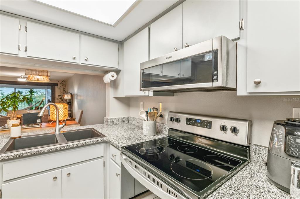 A kitchen features gray cabinets, granite countertops, a stainless steel stove, and a microwave — 90 S HIGHLAND AVENUE UNIT 402, TARPON SPRINGS, FL
