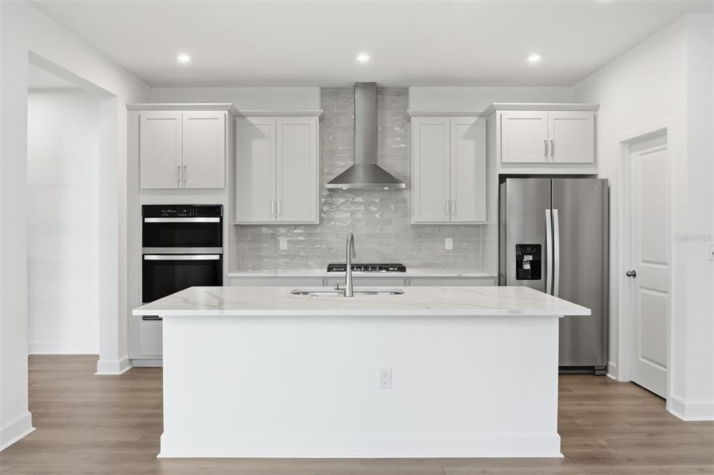 A modern kitchen features a white island, light gray cabinetry, stainless steel appliances, and tile backsplash — 1931 SEAWALL WAY, CELEBRATION, FL