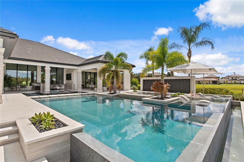 A modern house features a large swimming pool with a water feature and palm trees — 10521 BROADLAND PASS, THONOTOSASSA, FL