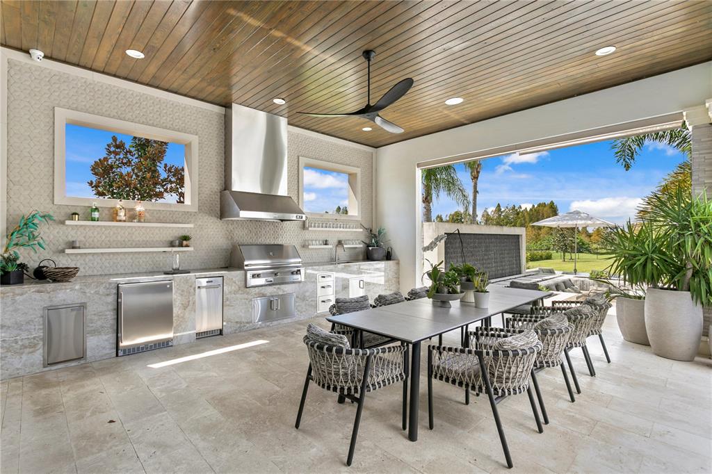 An outdoor kitchen and dining area features stone counters, stainless appliances, and a wood ceiling — 10521 BROADLAND PASS, THONOTOSASSA, FL