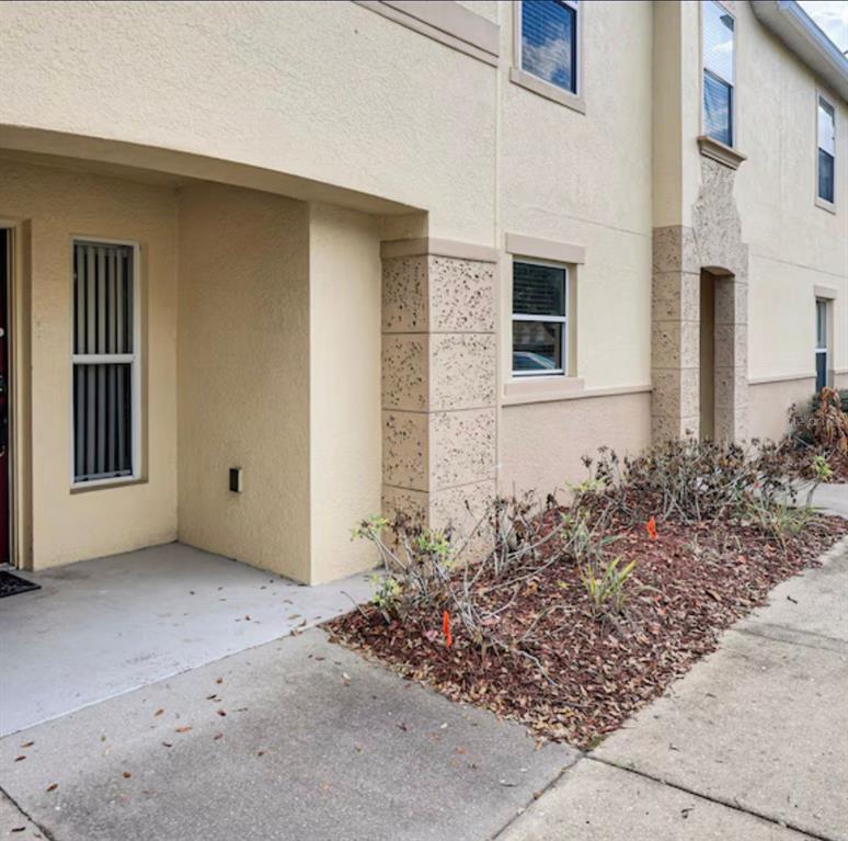 A beige stucco apartment building exterior with a concrete walkway and a small landscaped bed — 2704 CLUB CORTILE CIRCLE, KISSIMMEE, FL
