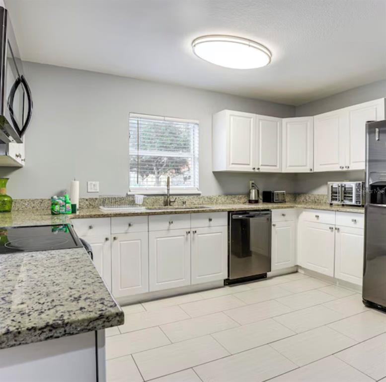 A kitchen features white cabinets, granite countertops, stainless steel appliances, and light-colored tile flooring — 2704 CLUB CORTILE CIRCLE, KISSIMMEE, FL