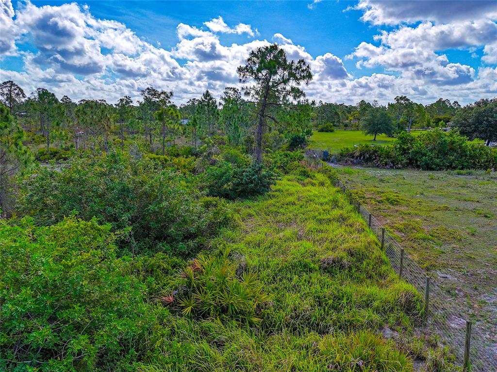 An aerial view of a grassy, partially wooded lot bordered by a wire fence — 8228 AUSTRIAN BOULEVARD, PUNTA GORDA, FL