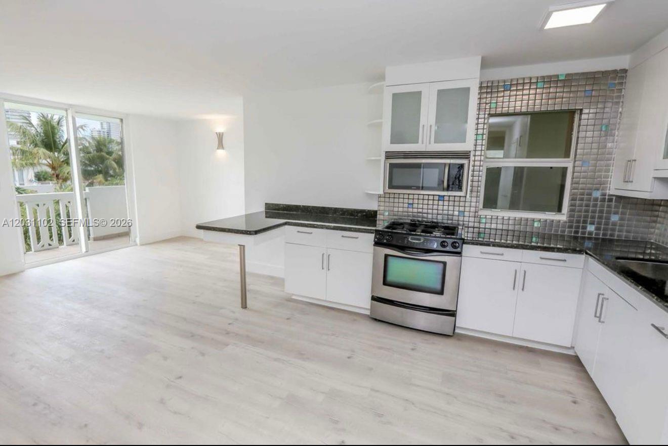 A kitchen with white cabinets, dark countertops, and stainless steel appliances opens to a living area — 301 Jefferson Ave # 3A, Miami Beach FL 33139, MIAMI BEACH, FL