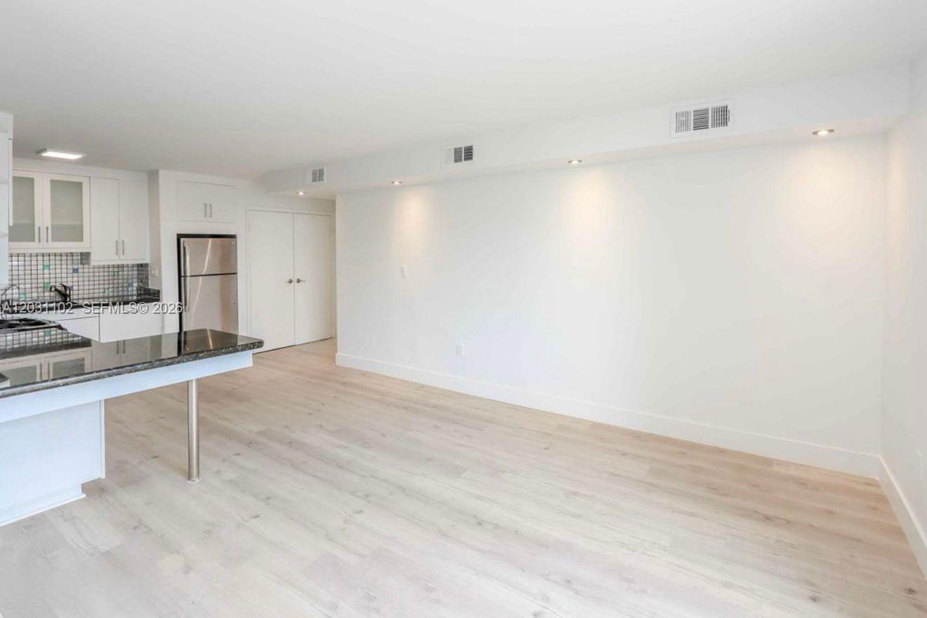 A kitchen with white cabinets and a breakfast bar opens into a spacious living area — 301 Jefferson Ave # 3A, Miami Beach FL 33139, MIAMI BEACH, FL