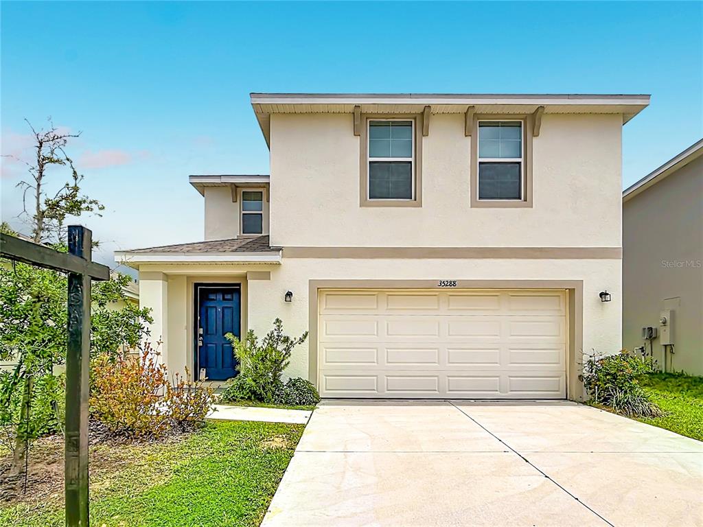 A two-story house with a beige stucco exterior, a blue front door, and a two-car garage — 35288 SPRUCE KNOB COURT, DADE CITY, FL
