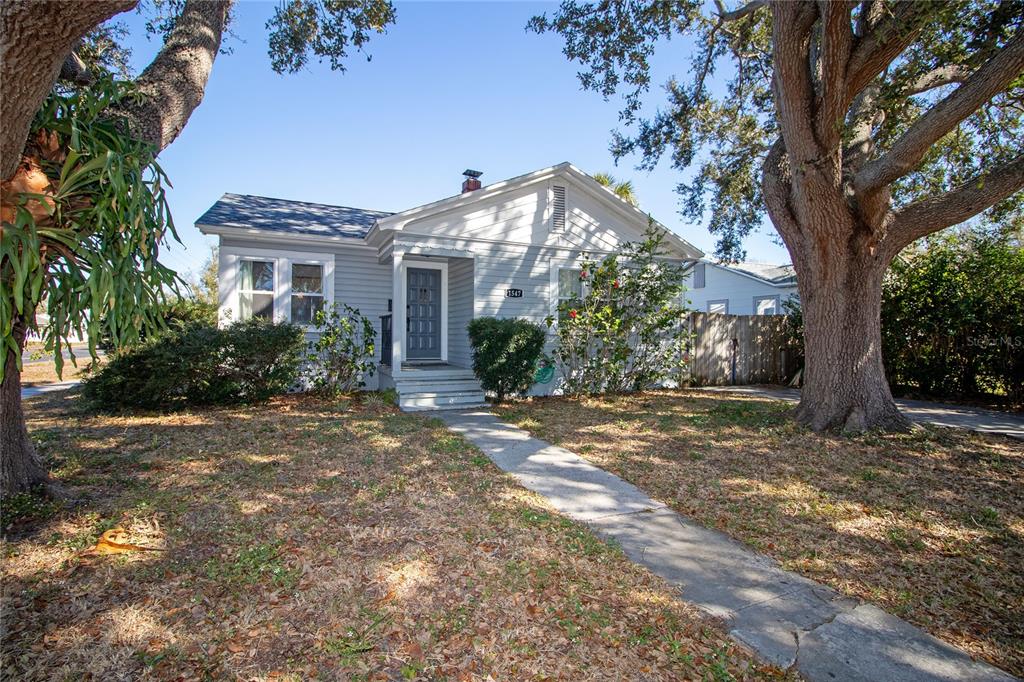 A single-story house with light gray siding and a front porch sits under large trees — 1547 35TH AVENUE N, ST PETERSBURG, FL