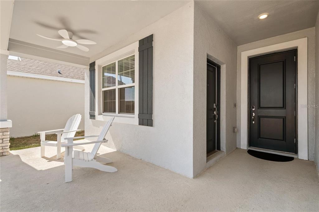 A covered front porch features two white Adirondack chairs, a window with shutters, and doors — 1172 TYLER LOOP, WINTER HAVEN, FL