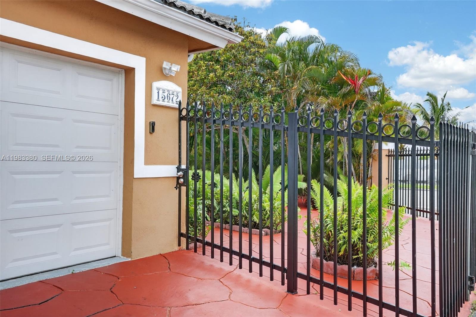 A black metal fence stands in front of a tan house with a garage — 15672 SW 91st Ln, Miami FL 33196, MIAMI, FL