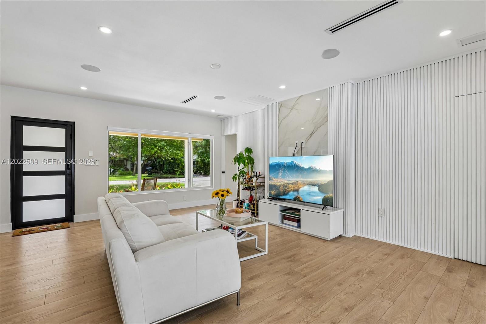 A living room features a white sofa, a television on a stand, and slatted walls — 5620 SW 63rd Ct, South Miami FL 33143, SOUTH MIAMI, FL