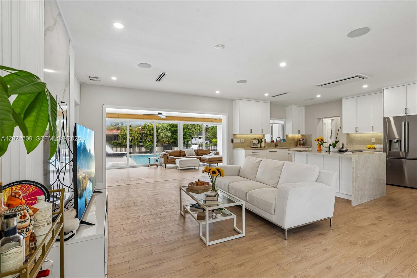 An open-concept living room and kitchen feature light wood floors and a view of a pool — 5620 SW 63rd Ct, South Miami FL 33143, SOUTH MIAMI, FL