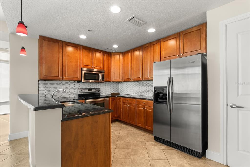 A kitchen features wood cabinets, black countertops, stainless steel appliances, and a tiled backsplash — 101 S EOLA DRIVE UNIT 1010, ORLANDO, FL